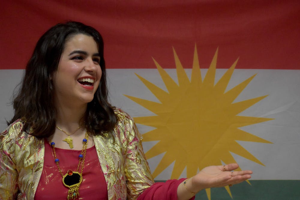 <p><span>Sara Zandy, 20, representing her culture wearing a jily kurdy in front of the Kurdish flag.</span></p>