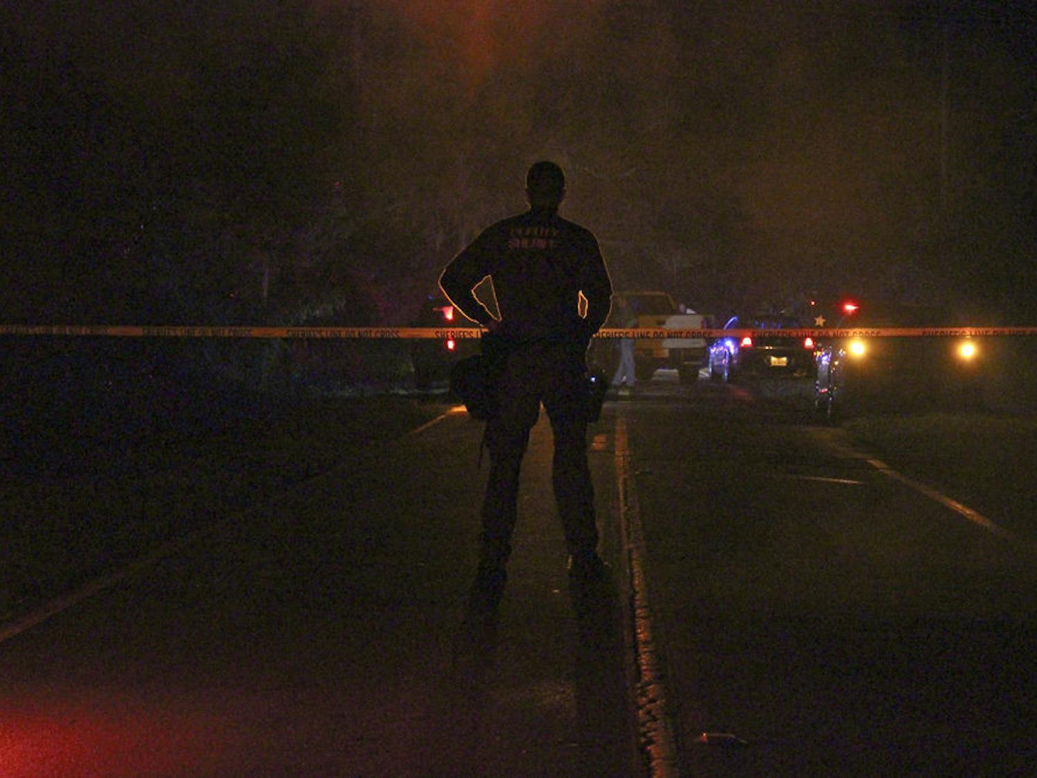 An officer with the Alachua County Sheriff’s office patrols the crime scene on Southeast Wacahoota Road on Tuesday night.