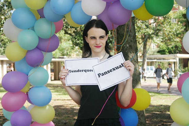 Logan Stallings, a 20-year-old psychology major, stands under a rainbow-colored balloon arch on the Plaza of the Americas Tuesday, identifying with both gender-queer and pansexual sexualities on National Coming Out Day. See story, page 4.