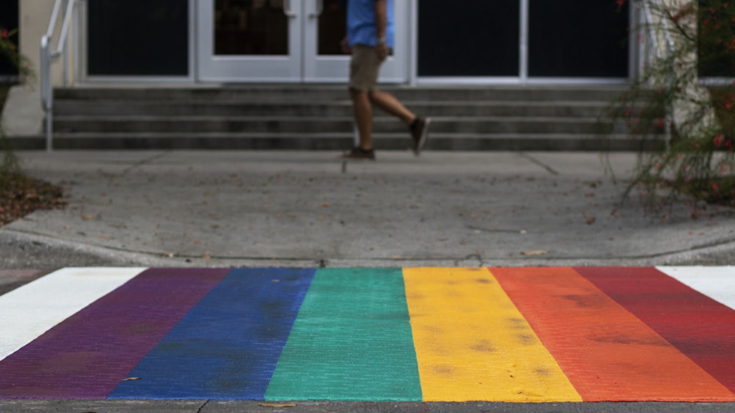 A pedestrian walks past one of the rainbow crosswalks Tuesday evening in downtown Gainesville near Bo Diddley Plaza.