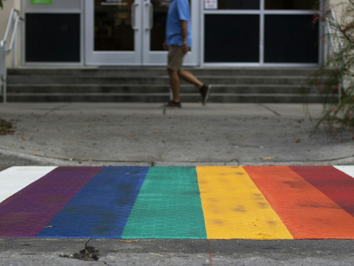 A pedestrian walks past one of the rainbow crosswalks Tuesday evening in downtown Gainesville near Bo Diddley Plaza.