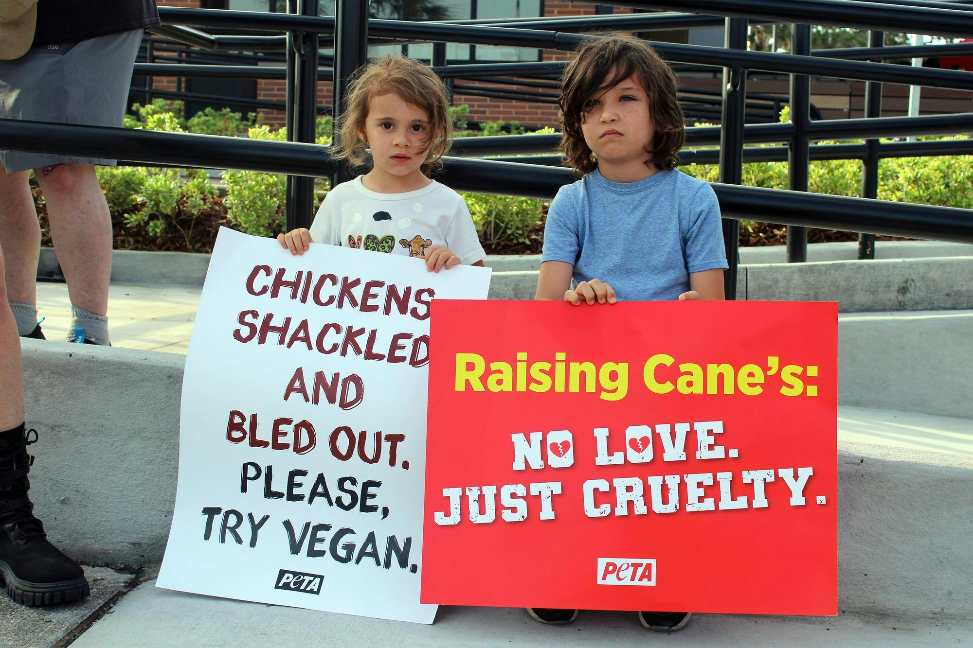 Sage Blair and Ezekiel Macallister sit while protesting the grand opening of Raising Canes, located at  12705 NW US HWY 441 in Gainesville, Fla., Wednesday, May 27, 2026.
