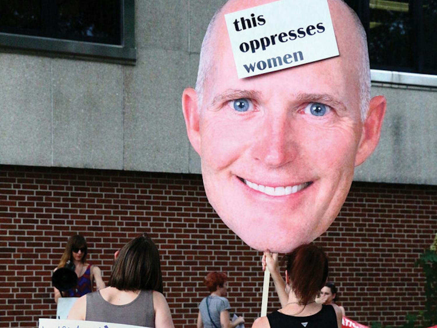 Brooke Eliazar-Macke (left), 32, and Regan Garner (right), 41, both members of the National Women's Liberation, hold signs at the Rally and Speak Out against Rick Scott's Policies event in downtown Gainesville on Friday on the corner of University Avenue and Main Street. The Speak Out event organized by the National Women's Liberation gives women a political opportunity to share their personal experiences.