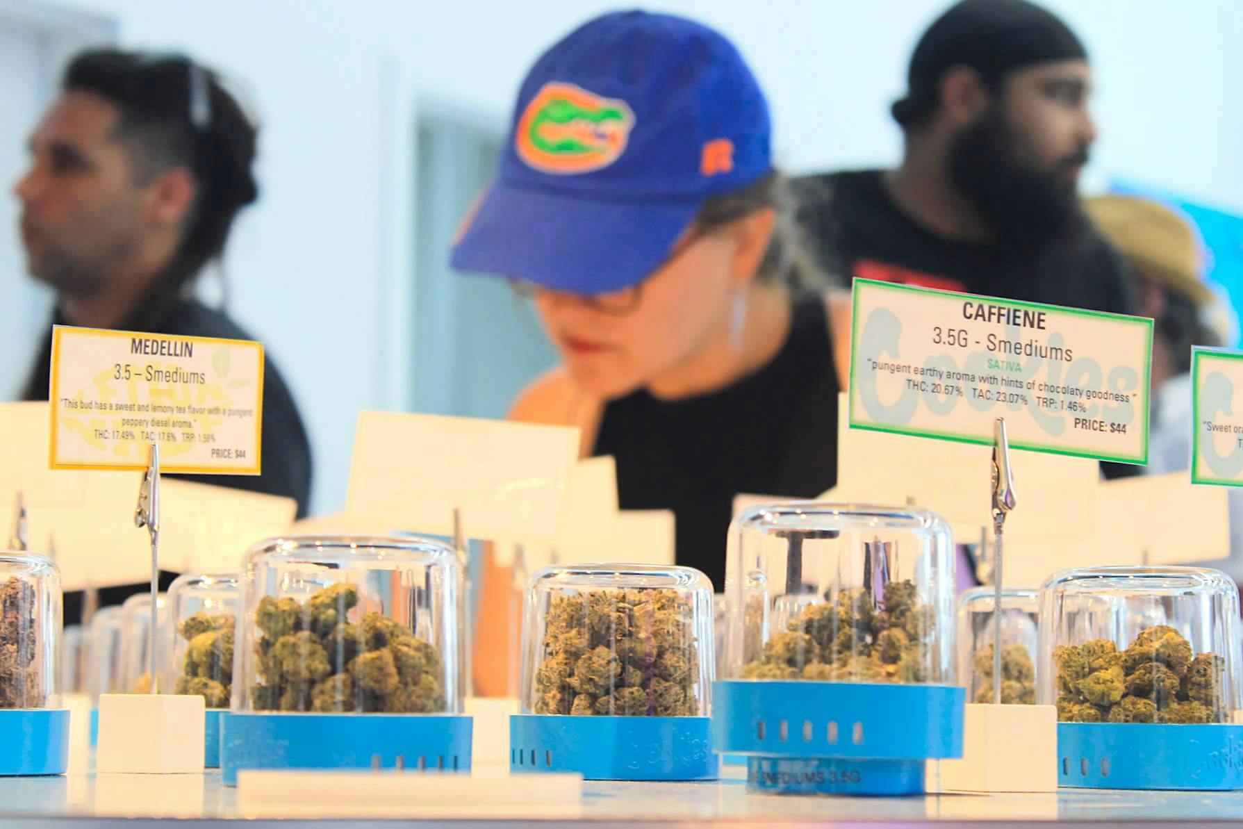 Customers gather around the &quot;bud bar,&quot; a round table showcasing dozens of cannabis strains at Cookies on Saturday, July 1, 2023. ﻿