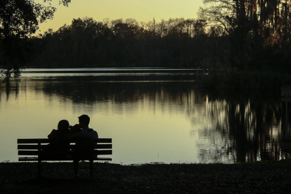Summer Levinson, a 21-year-old UF marketing senior, and Robert Matias, a 21-year-old UF chemical engineering senior, eat sandwiches and watch the sunset over Lake Alice Saturday. The view was a change of pace from eating in front of the TV, Matias said.