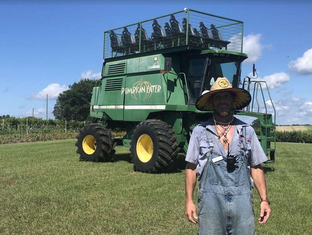 <p>Steven Keiper stands in front of the Pumpkin Eater, a machine that gives guests a view of the peach festival at Red White and Blue Farm from 30 feet in the air, on Saturday, May 28 2022.</p>