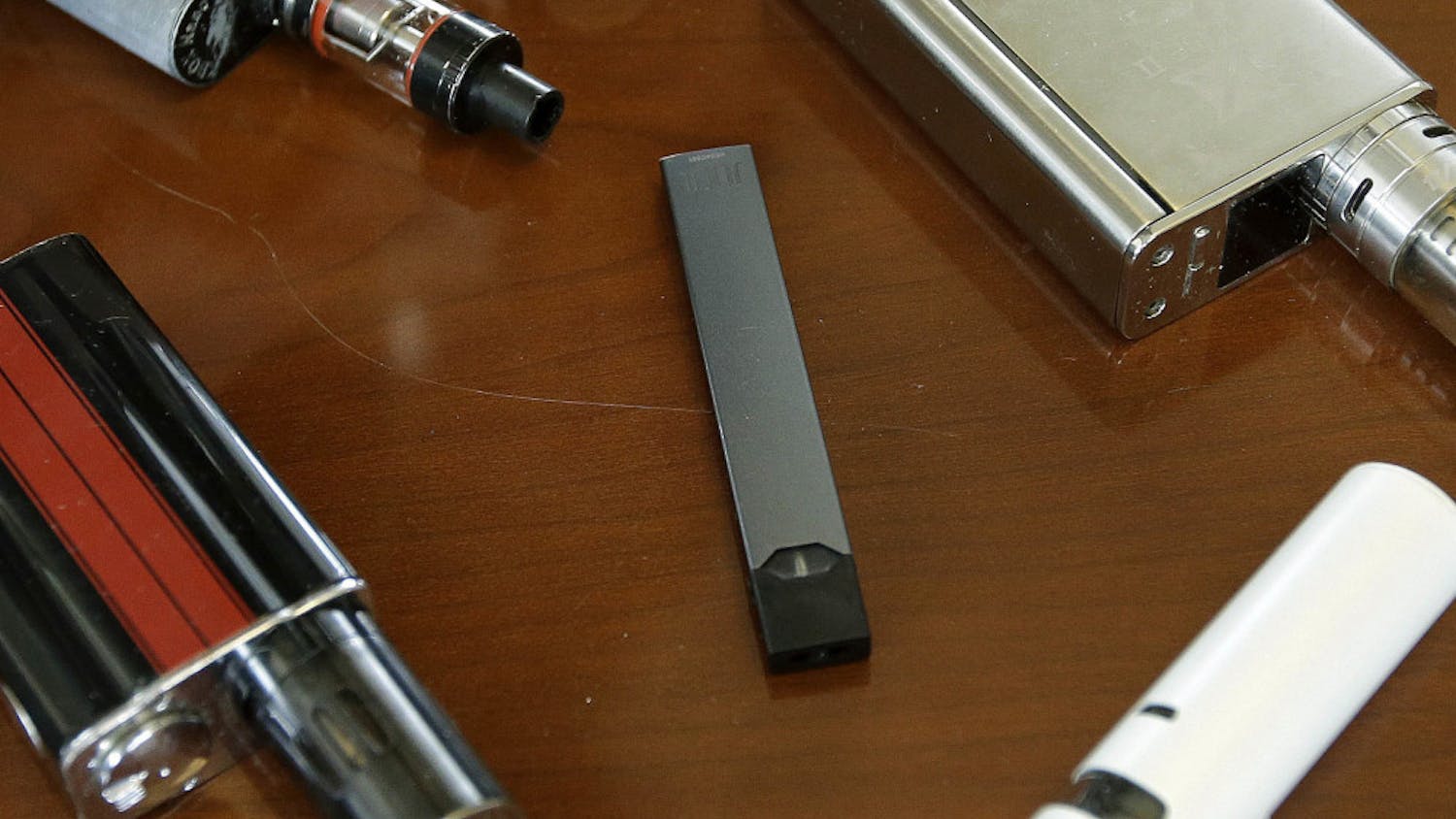 This Tuesday, April 10, 2018 file photo shows vaping devices, including a Juul, center, that were confiscated from students at a high school in Marshfield, Mass. On Tuesday, Nov. 13, 2018, San Francisco-based Juul Labs Inc. announced it had stopped filling orders for its mango, fruit, creme and cucumber pods but not menthol and mint. It will sell all flavors through its website and limit sales to those 21 and older. (AP Photo/Steven Senne)
