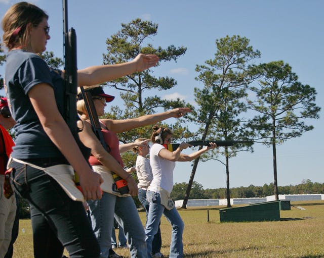 A group of women participating in the NRA Women on Target Instructional Shooting Clinic aim toward a moving clay disk at the Gator Skeet and Trap Club.