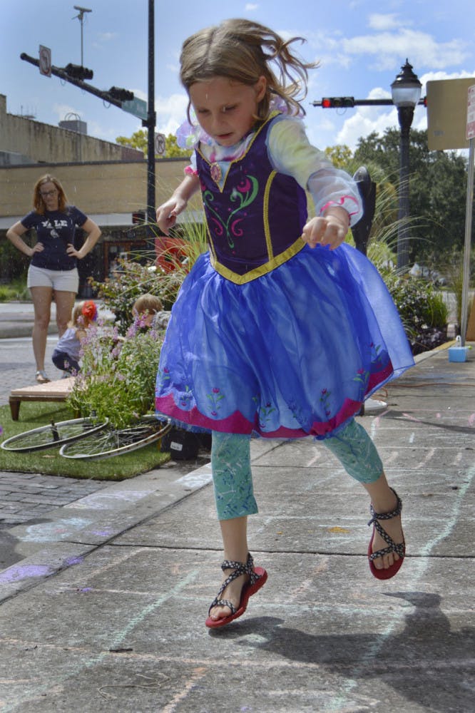 PARKING DAY PRINCESS -- Juniper Eddleton, 5, jumps into a game of hopscotch during (PARK)ing Day Saturday on the corner of Northeast First Avenue and Main Street. UF’s chapter of America's Society of Landscape Architects set up “pop-up parks” downtown this weekend to promote more public, green space in the urban environment.