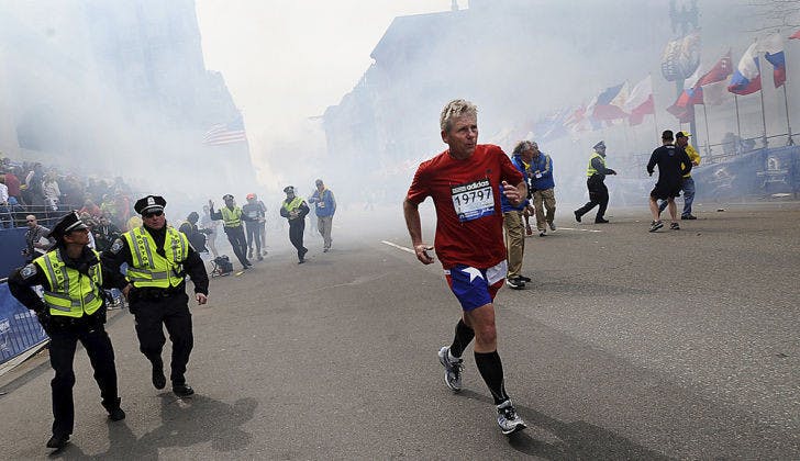 A Boston Marathon competitor and Boston police run from the area of an explosion near the finish line in Boston on Monday. (AP Photo/MetroWest Daily News, Ken McGagh)