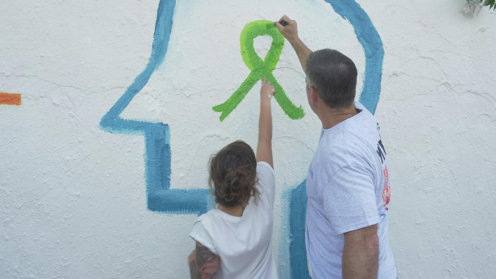 Laura Martin, 28, a peer support specialist at UF Health and Joe Munson, Director of Clinical Services at UF Health, paint the mental health awareness ribbon together on the mural at Southwest 34th Street.
