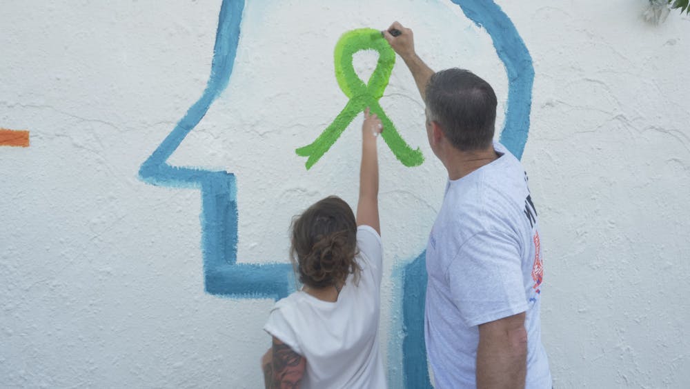 <p>Laura Martin, 28, a peer support specialist at UF Health and Joe Munson, Director of Clinical Services at UF Health, paint the mental health awareness ribbon together on the mural at Southwest 34th Street.</p>