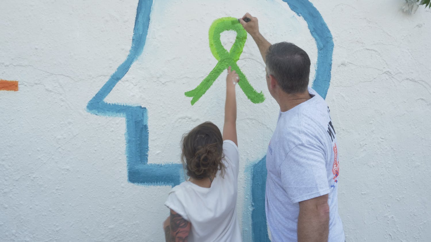 Laura Martin, 28, a peer support specialist at UF Health and Joe Munson, Director of Clinical Services at UF Health, paint the mental health awareness ribbon together on the mural at Southwest 34th Street.