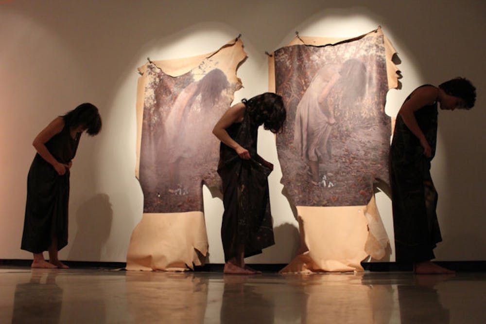 <p>Three performance artists pose in front of portraits printed on leather on display at Naomi Fisher’s reception for “Lay of the Land” at the University Gallery on Friday.</p>