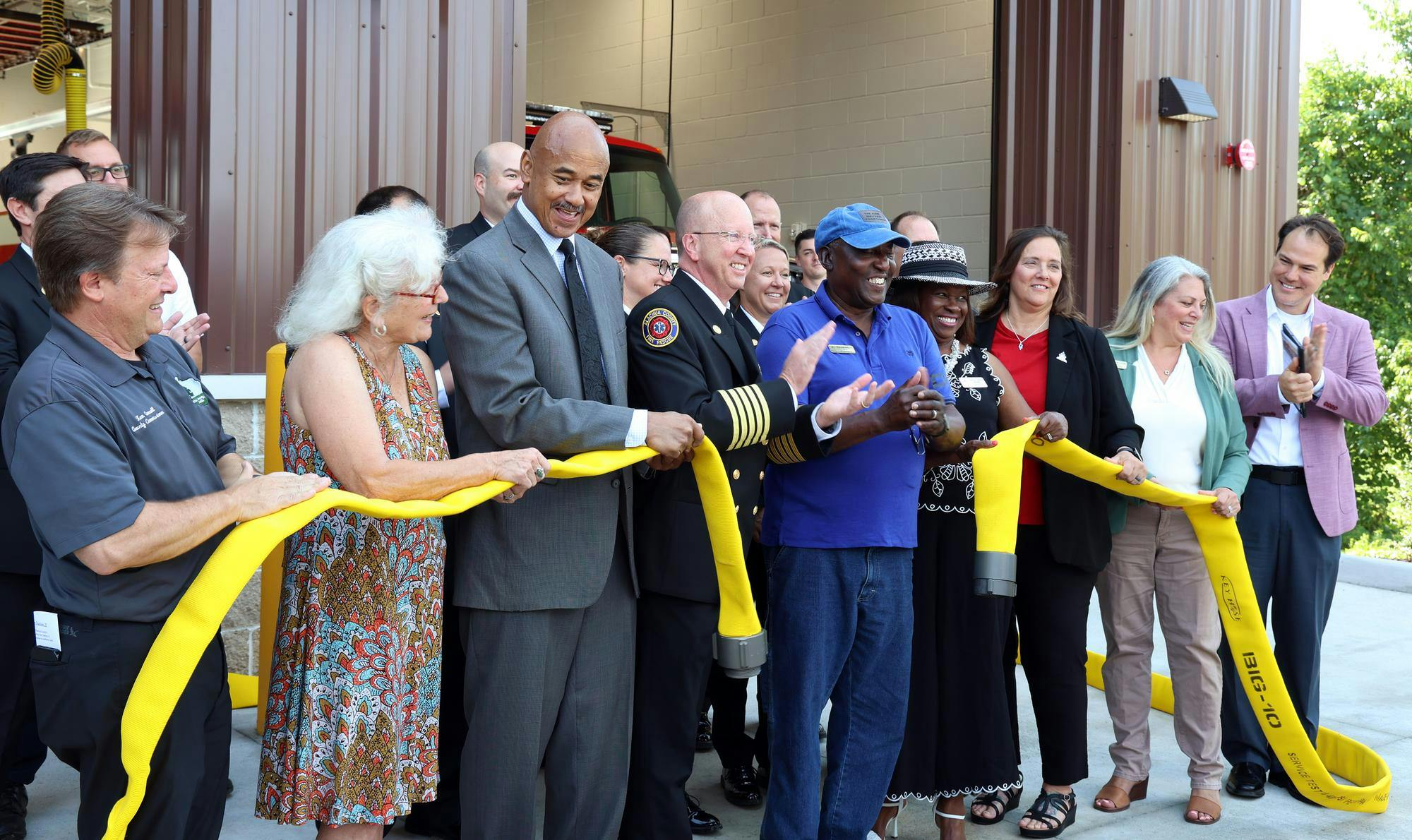 Alachua County Fire Rescue Chief Harold Theus (center left) and Alachua Mayor Walter Welch (center right) clap after ceremonially unscrewing a firehose to mark the grand opening of Fire Station 21 in Alachua, Fla., on Friday, May 30, 2025.
