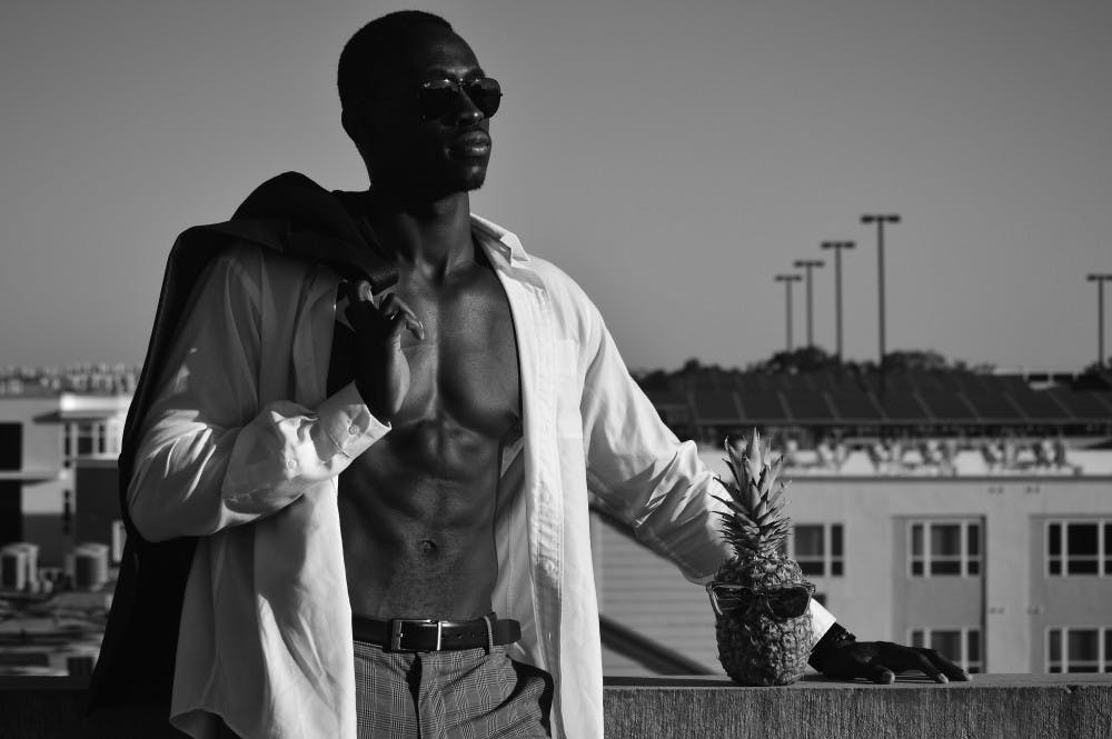 UF biology junior Taiwo Alonge, 21, and George the Pineapple pose atop a roof at sunset. George has found fame on the Instagram account peopleandapineapple.