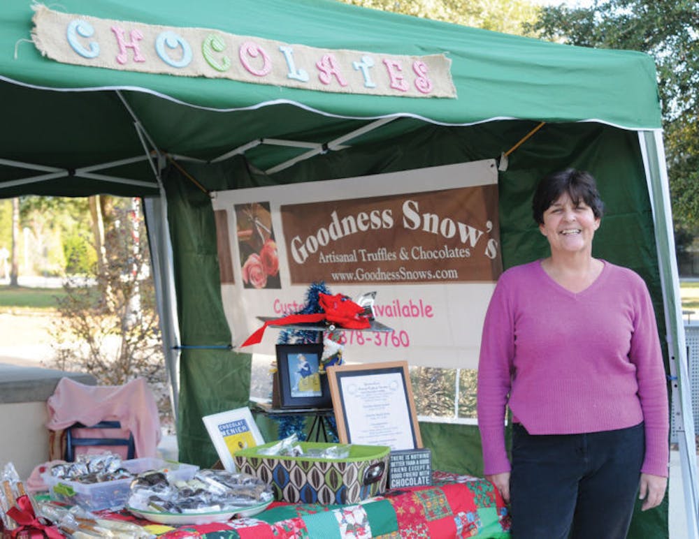 <p>Gwen Thompson, owner of Goodness Snow’s, smiles next to the stand she and her husband sell their chocolates from. They frequently set up shop in the Tioga Town Center from 3 to 6 p.m. on Monday afternoons.</p>