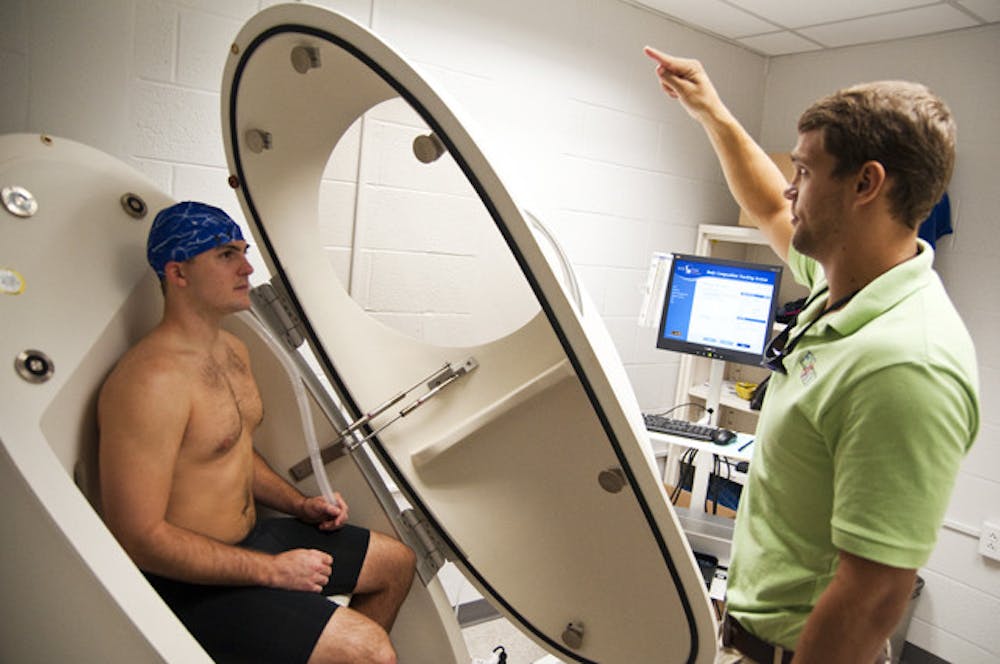 <p>Food science graduate student Adam Knox, 23, sits in the Bod Pod as nutrition graduate student Blake Bartholomew, 23, explains how to use the breathing tube inside of the pod in order to properly calculate total body fat percentage.</p>