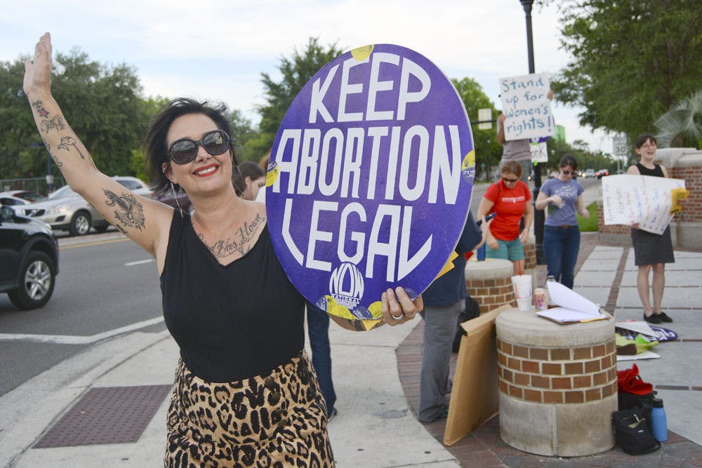 <p>Su Mendez, an activist with the National Organization for Women and National Women’s Liberation, holds a sign and waves at passing vehicles at an abortion rights protest on University Avenue and 13th Street on Tuesday.</p>