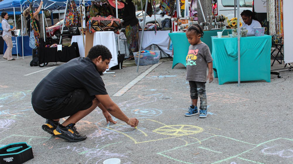 <p>A resident draws chalk with a child in front of vendor tables and tents at the Revolution Before Evolution Festival Sunday, Nov. 27﻿, 2022.</p>