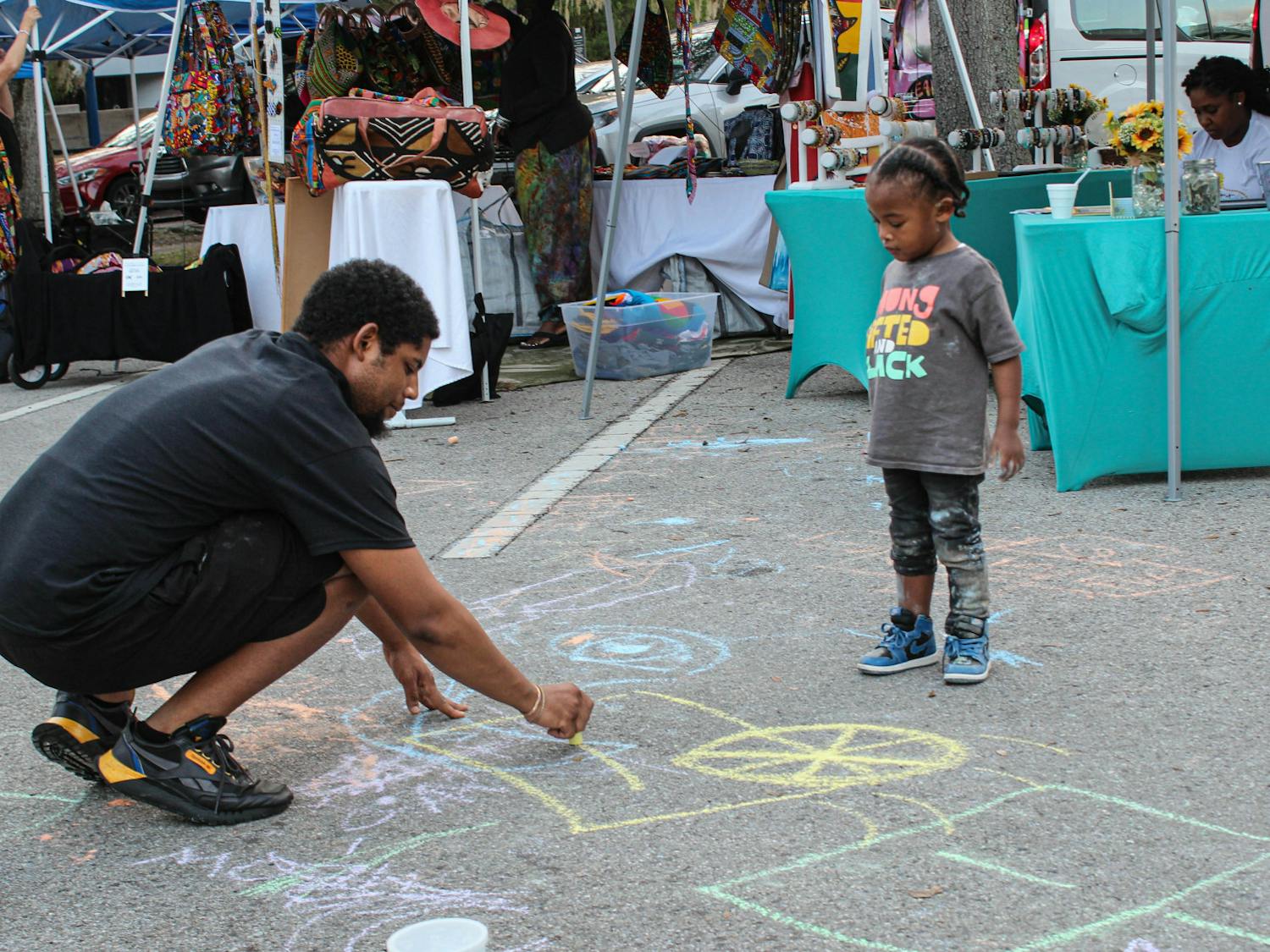 A resident draws chalk with a child in front of vendor tables and tents at the Revolution Before Evolution Festival Sunday, Nov. 27, 2022.