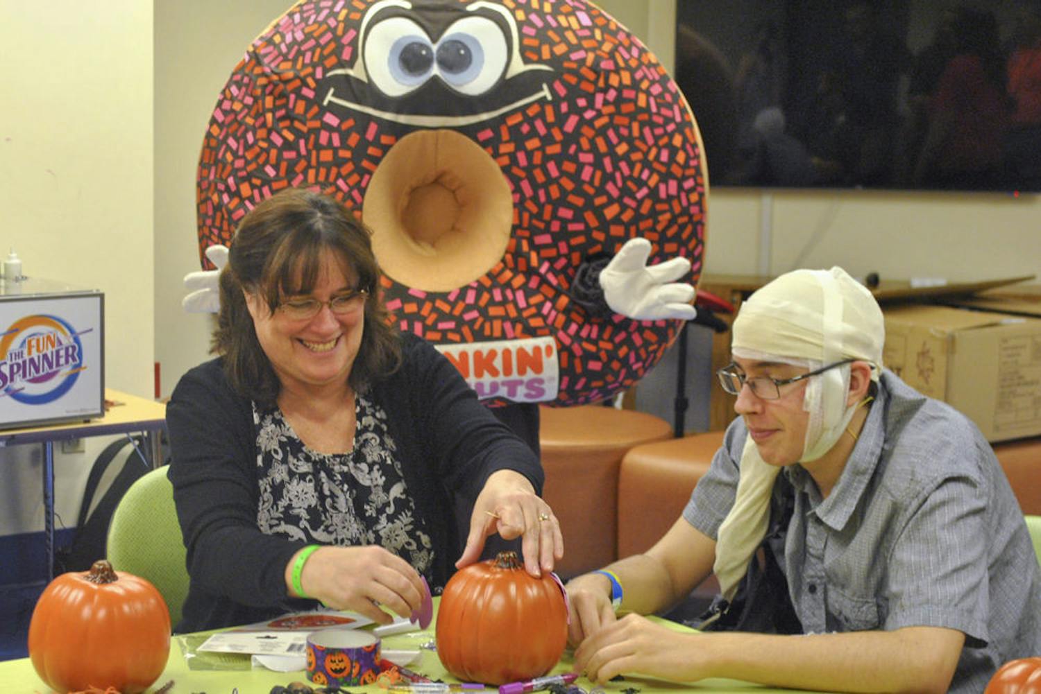 Andrew Weatherly (right), 17, decorates his plastic pumpkin with his mom while Sprinkles, the Dunkin’ Donuts mascot, poses.