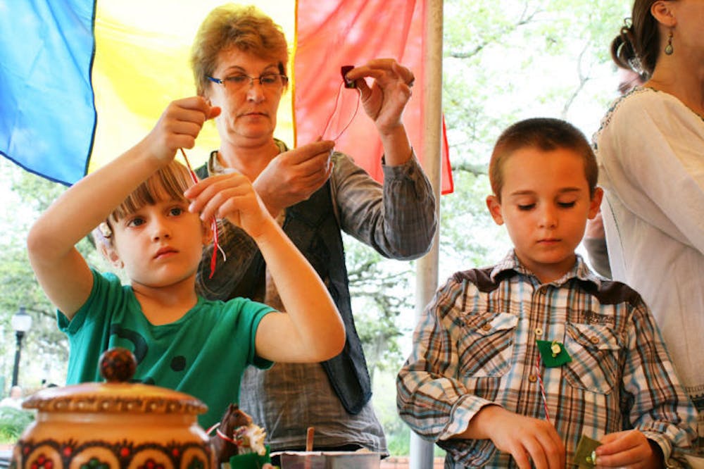 <p>Camelia Moisescu, of Romania, makes martisors with her grandchildren — Stefanie, 6, and Michael, 8 — at the Viva Europe! festival in downtown Gainesville on Saturday. Women wear these pins during March to symbolize the coming of spring.</p>