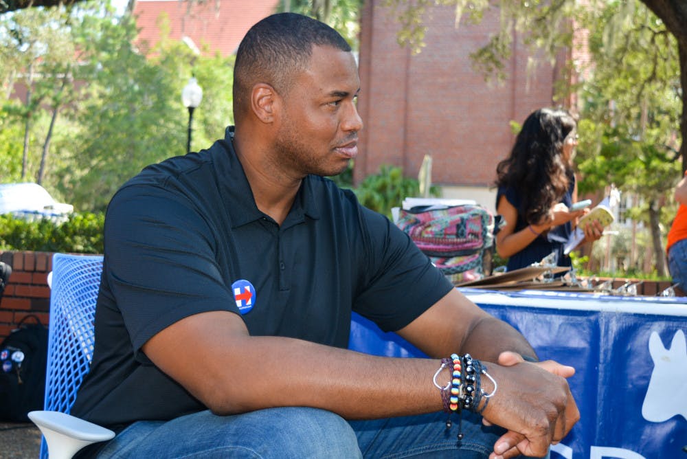 Jason Collins sits in front of the UF College Democrats table on Turlington Plaza on Friday. Collins, along with students, registered people to vote and campaigned for Hillary Clinton.