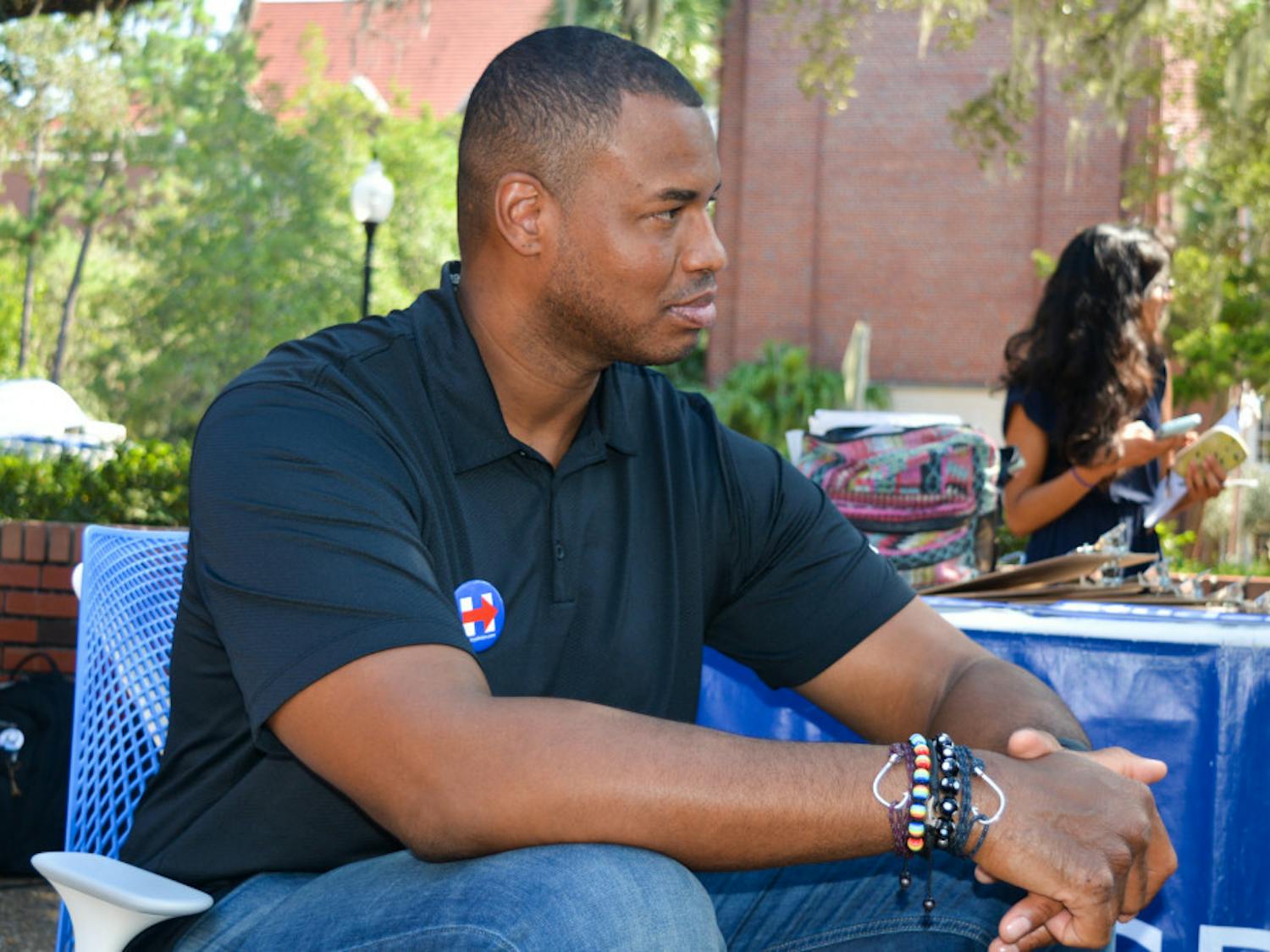 Jason Collins sits in front of the UF College Democrats table on Turlington Plaza on Friday. Collins, along with students, registered people to vote and campaigned for Hillary Clinton.