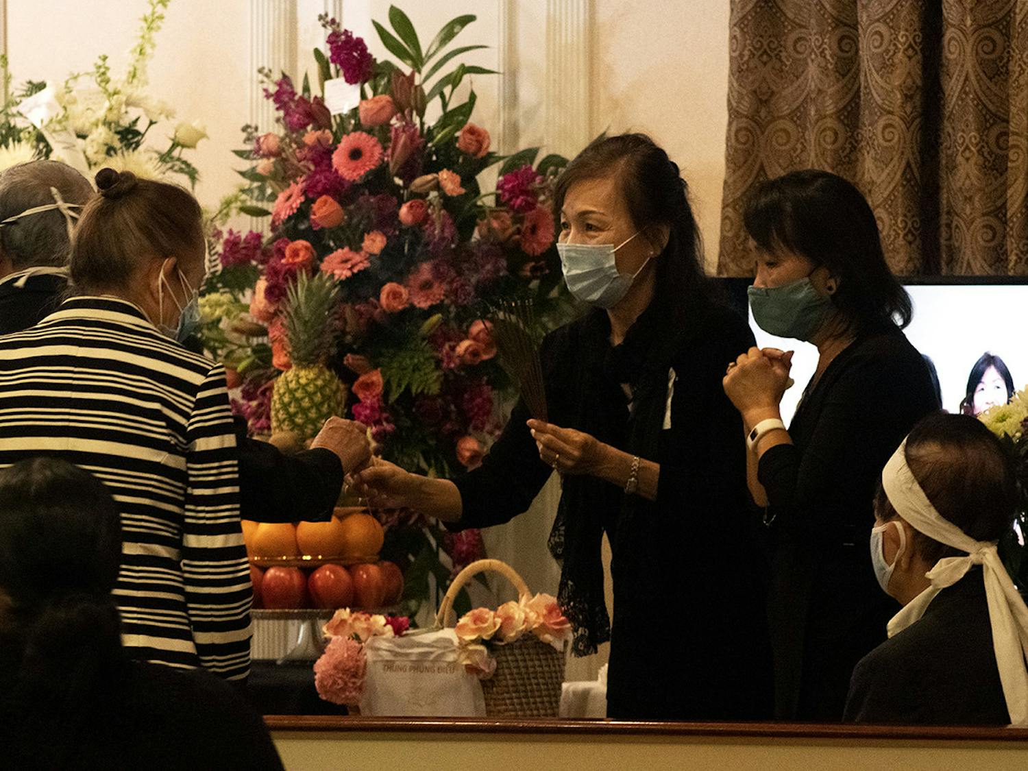 Two people hand out sticks of incense during the funeral of Bach Lien Tong Duong on Wednesday, April 14, 2021. Duong was a volunteer who taught Vietnamese at UF before an official position was created and played a significant role in creating the annual Pho fundraiser for the Vietnamese Student Organization before she passed away.