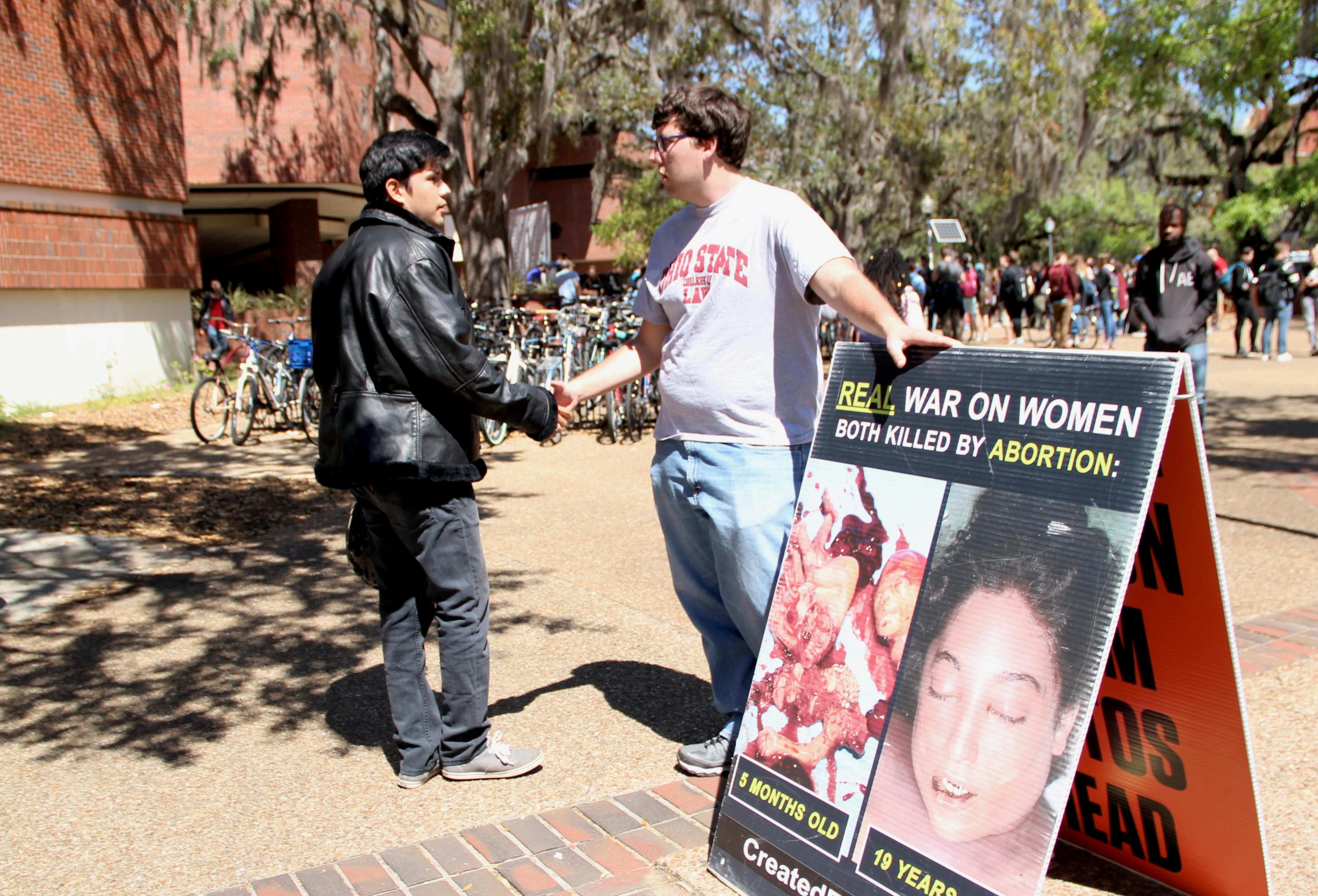 Alfredo Patiño, 22, a UF senior political science and sociology major, and Joe Trammel, 22, a law student from Ohio State University and member of the Created Equal organization, shake hands. Patiño and Trammel had a respectful conversation about the images the Created Equal organization placed on Turlington Plaza on Tuesday.