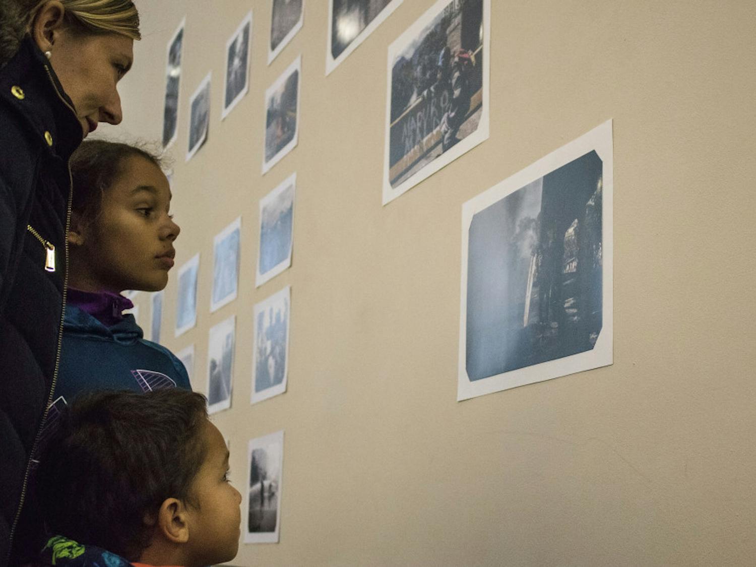 Georgia Bianchi, 41, and her children Eva Bailey, 9, and Christopher Bailey, 4, look at photos Wednesday by Venezuelan photographer Andres Avellaneda on display in the Santa Fe College Fine Arts Hall. The gallery was arranged by various Santa Fe clubs to raise funding for Avellaneda’s U.S. visa application fees.