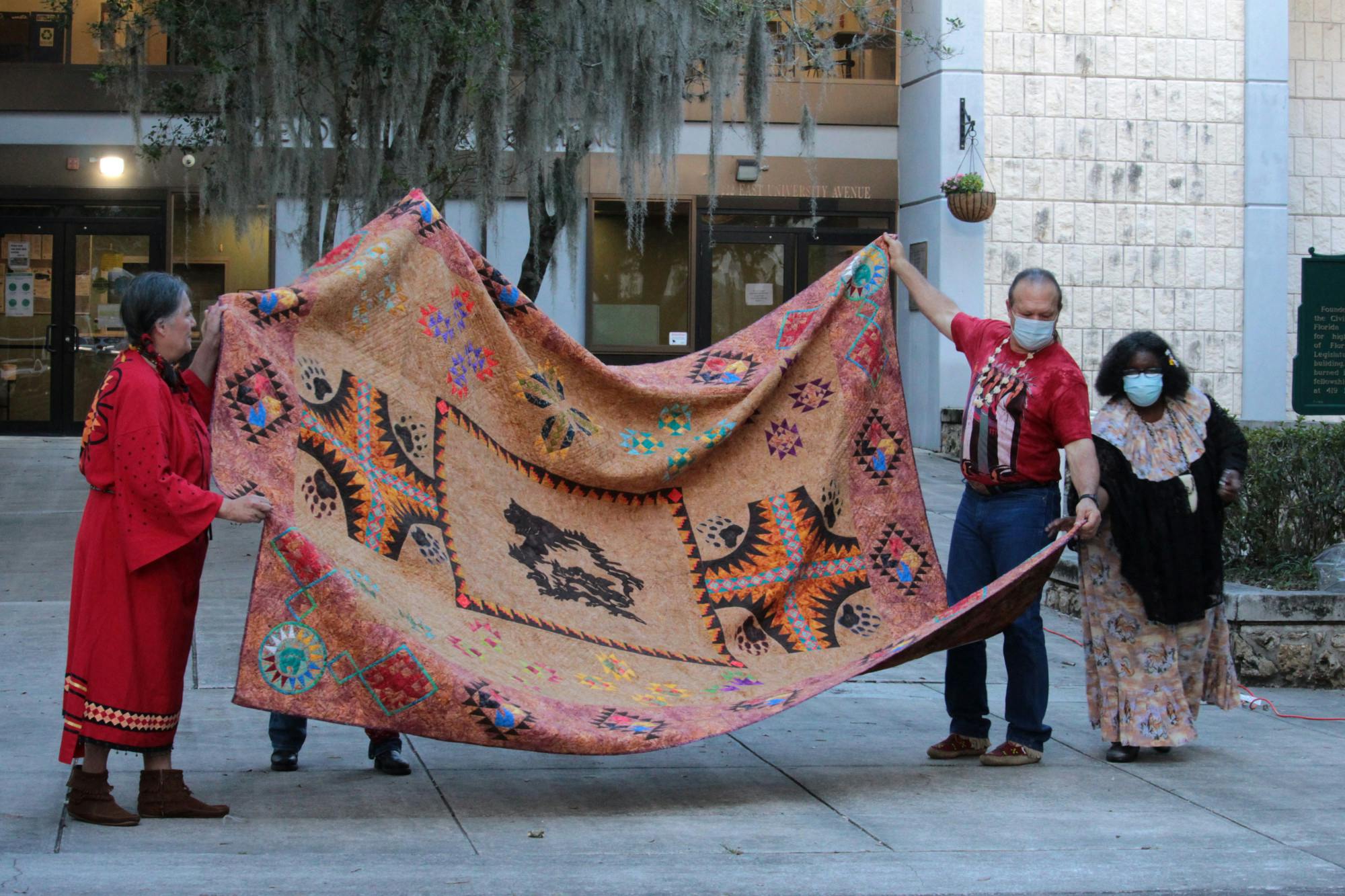 Dave Trezak (second from the right), Sioux tribe, helps to display a handmade, Native American quilt at Gainesville City Hall on Monday, Oct. 11, 2021. 