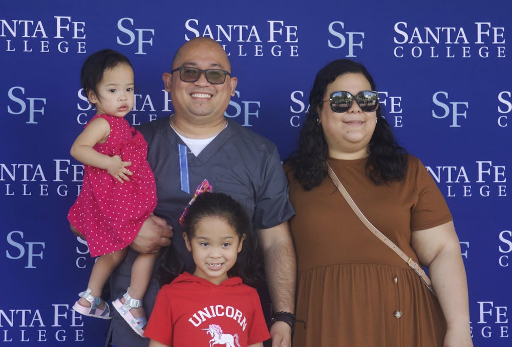 Shariff Manlosa (second from the left) stands on the graduation stage at Santa Fe College's Drive-Thru Grad Walk with his daughters, Monina (left) and Sofia (third from the left), and his wife, Margarita (right) on Thursday, April 29, 2021.