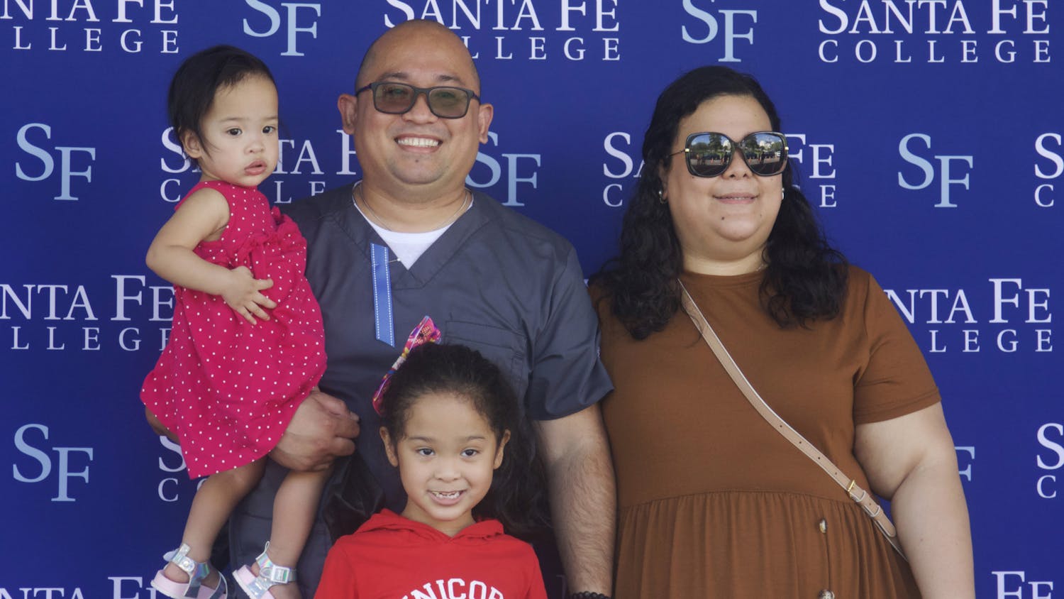 Shariff Manlosa (second from the left) stands on the graduation stage at Santa Fe College's Drive-Thru Grad Walk with his daughters, Monina (left) and Sofia (third from the left), and his wife, Margarita (right) on Thursday, April 29, 2021.