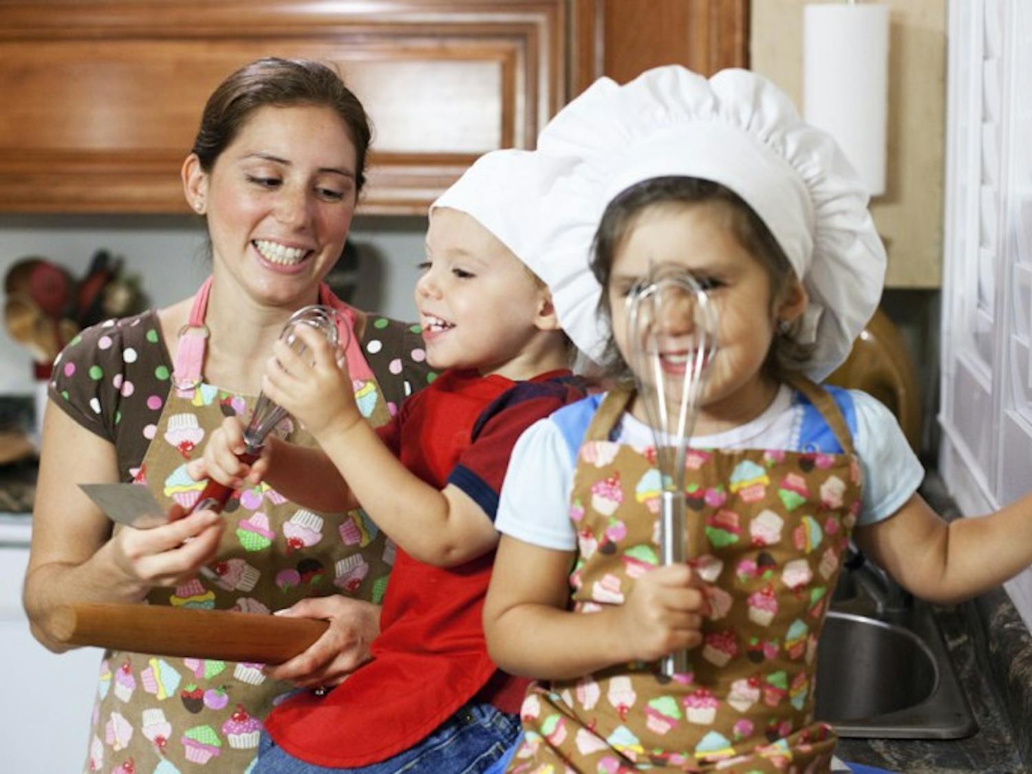Sherrie Blackwelder’s children Isabella, 4, and Ira, 2, wield their favorite baking utensils with their mother on Monday night at their home in Gainesville. Blackwelder makes cakes and other desserts out of her home for her business, Cake Classics.