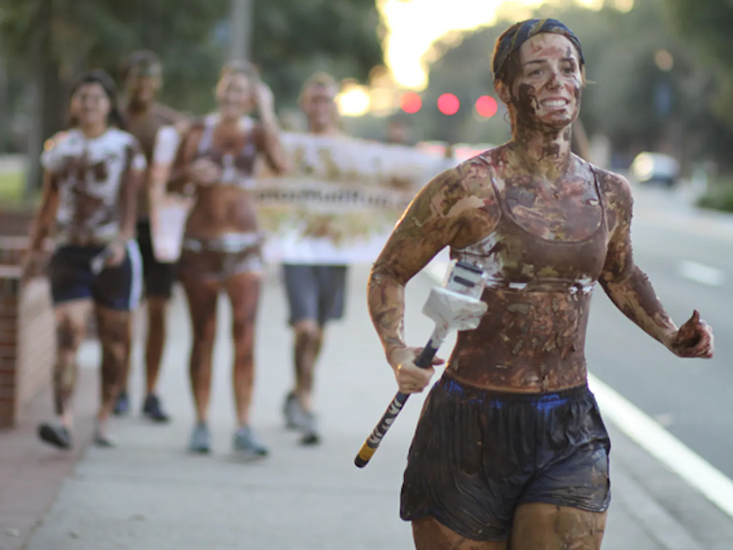 Mud-splattered Chantel Carter, 23, runs along University Avenue with four friends Tuesday evening promoting Gator Mud Run, a 5K race and paramilitary-style obstacle course on Nov. 6.