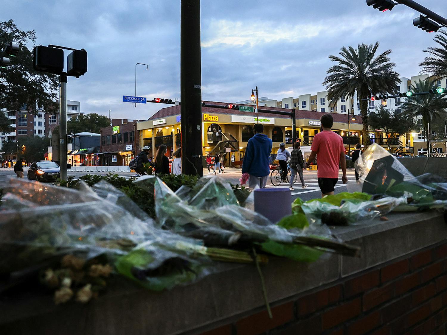 Pedestrians cross West University Avenue on Wednesday, Feb. 17, 2021, near a memorial at the site of a car crash that killed Sophia Lambert, a UF student, in January.