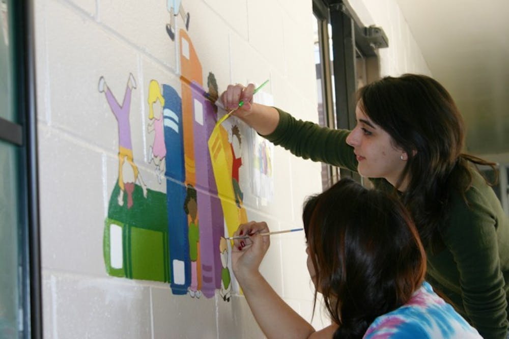 <p>Lesly Parra, an 18-year-old advertising freshman, and Sasha Saigol, a 19-year-old marketing freshman, perfect a mural in a Chester Shell Elementary School hallway Saturday. They volunteered their time as a part of Project Makeover, an organization that fixes up one Alachua County school each year.</p>