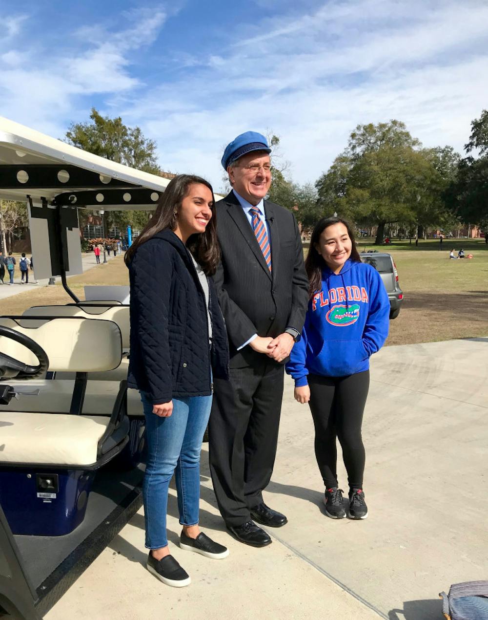 <p>UF President Kent Fuchs poses with students in front of his Gator-themed golf cart. He drove students back and forth between campus locations on the first day of classes. </p>