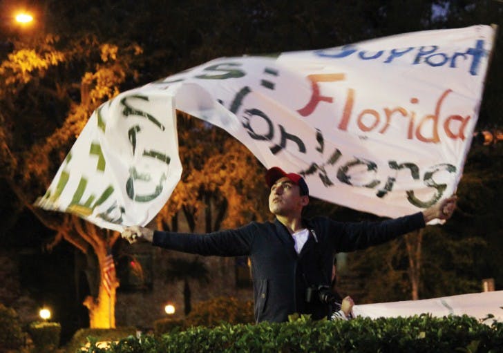 Julio Mora, a 22-year-old architecture junior, hoists a banner that reads, “Expand Support Ethics: Florida Farm Workers,” at a protest by the Interfaith Alliance for Immigrant Justice group at the Publix on 34th Street and University Avenue Monday night.