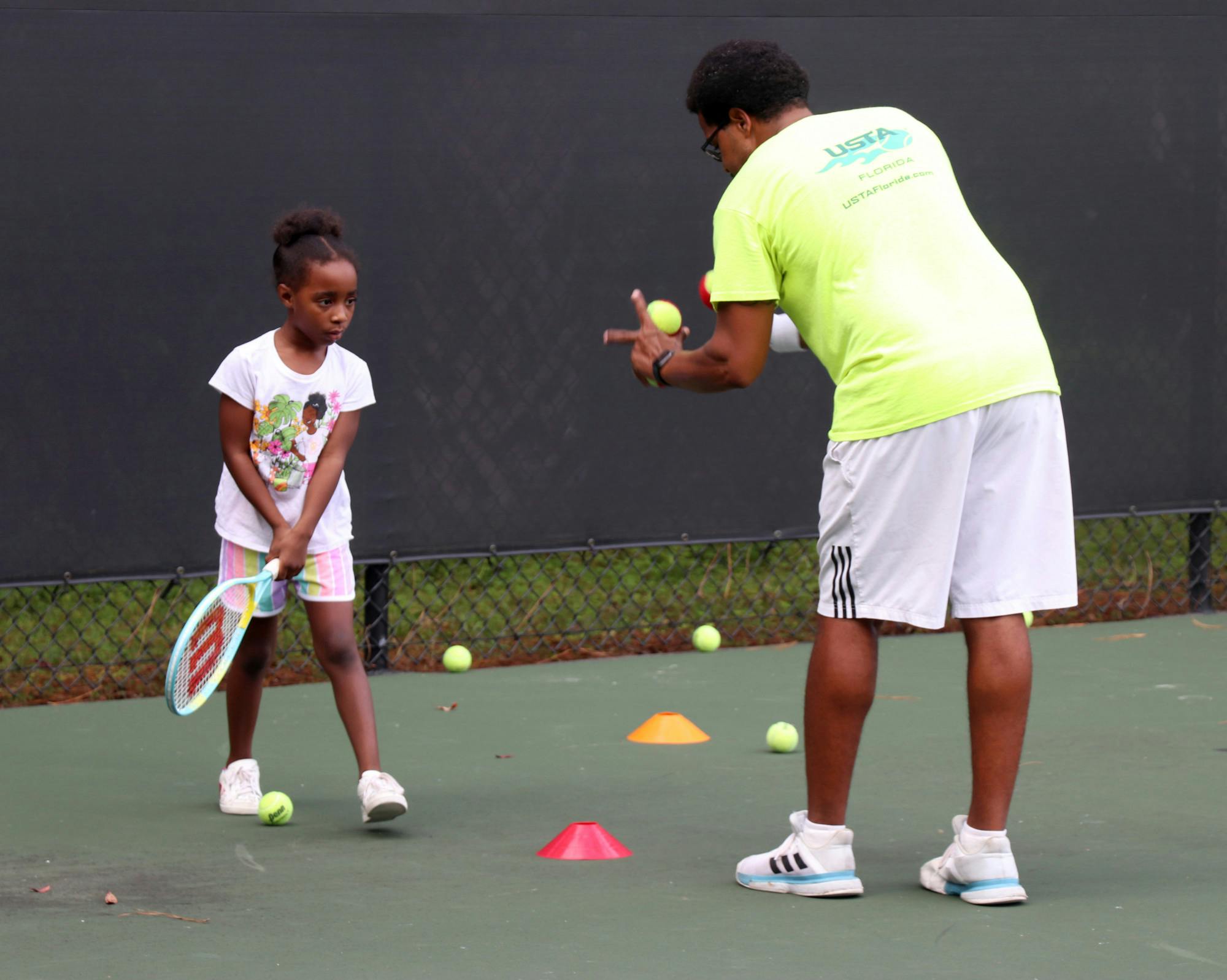 Lainey Norton (left), 6, attends a tennis lesson led by Christopher Scott Champion (right), 35, during the program at T.B. McPherson Park on Thursday, Sept. 23, 2021. The pilot program offers discounted lessons for East Gainesville residents. 
