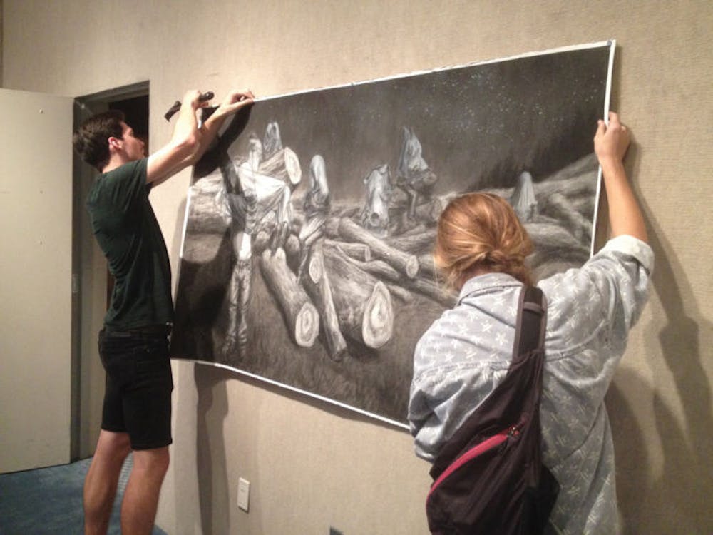 <p>Zac Thompson and Hannah Dwyer hang a drawing for the “Quarantined” exhibition inside the Gallery at the Reitz Union. The opening reception is from 7 to 9 p.m., and their work will be on display through Dec. 5.</p>