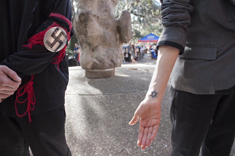 <p><span id="docs-internal-guid-b67cf575-de15-9cd5-f78d-6633e4df68bb"><span>Michal Katz (right), an administrative worker at the UF Dean’s Office, displays her Star of David tattoo while standing next to Michael Dewitz (left), who wears a swastika on his sleeve near Turlington Hall. Students surrounded Dewitz, yelling at him and holding signs in front of his face, for about four hours</span> <span>on Thursday</span><span>.</span></span></p>