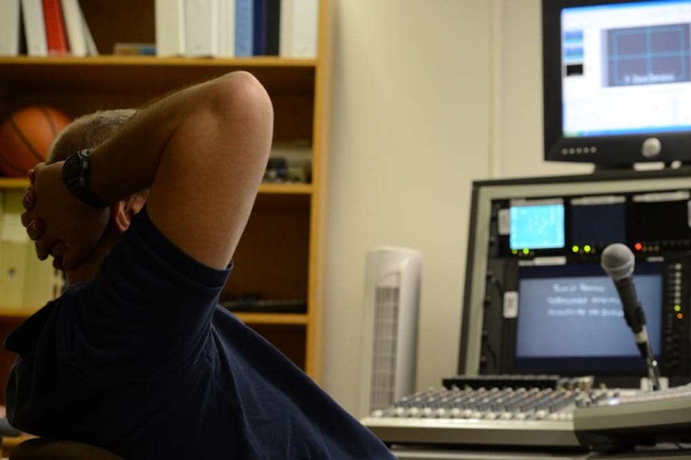 <p>Anthony Bouton, known to most as “The Director,” lounges at his control panel as he films professor Mark Rush’s microeconomics class Friday morning.</p>