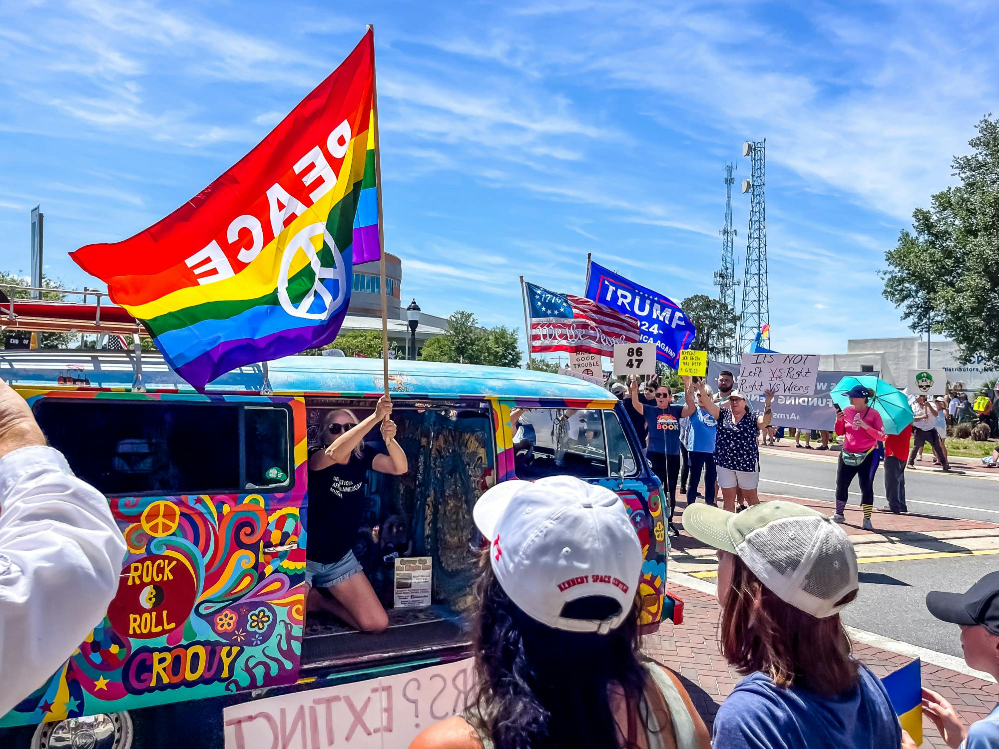 A protester waves a rainbow “Peace” flag from a bright painted Volkswagen van on Saturday, April 5, 2025.
