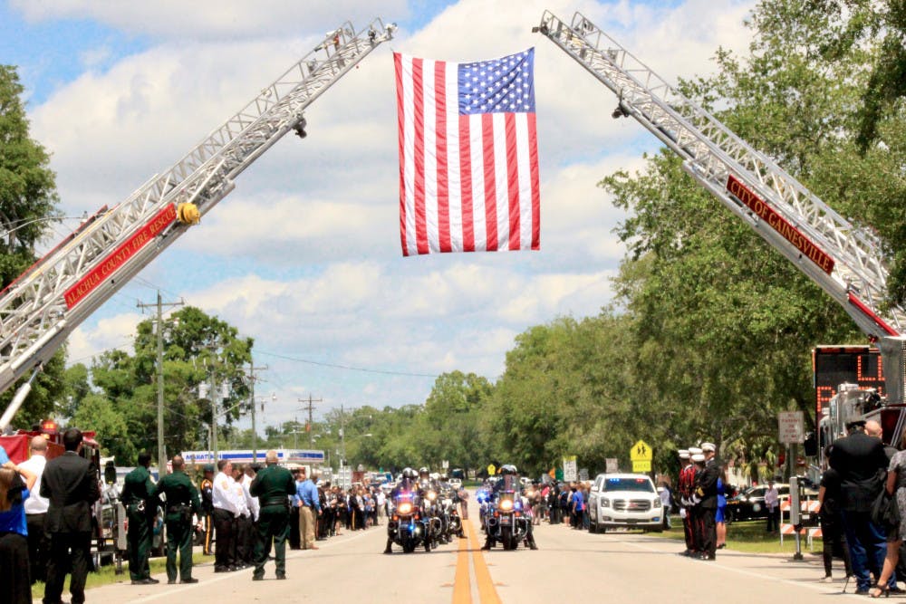 <p>A group of law enforcement officers drive under the U.S. flag hoisted by Alachua County Fire Rescue and Gainesville Fire Rescue fire engine ladders as part of the funeral procession on South Main Street in Bell, Florida for the two deputies who were shot in Trenton.</p>