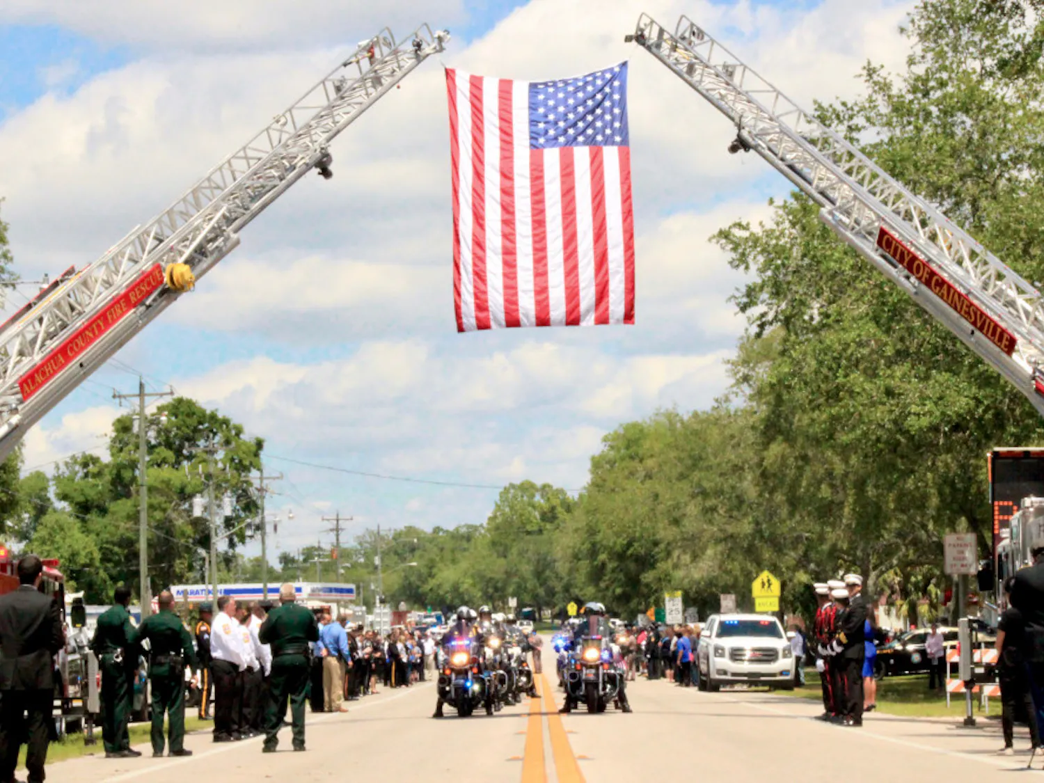 A group of law enforcement officers drive under the U.S. flag hoisted by Alachua County Fire Rescue and Gainesville Fire Rescue fire engine ladders as part of the funeral procession on South Main Street in Bell, Florida for the two deputies who were shot in Trenton.