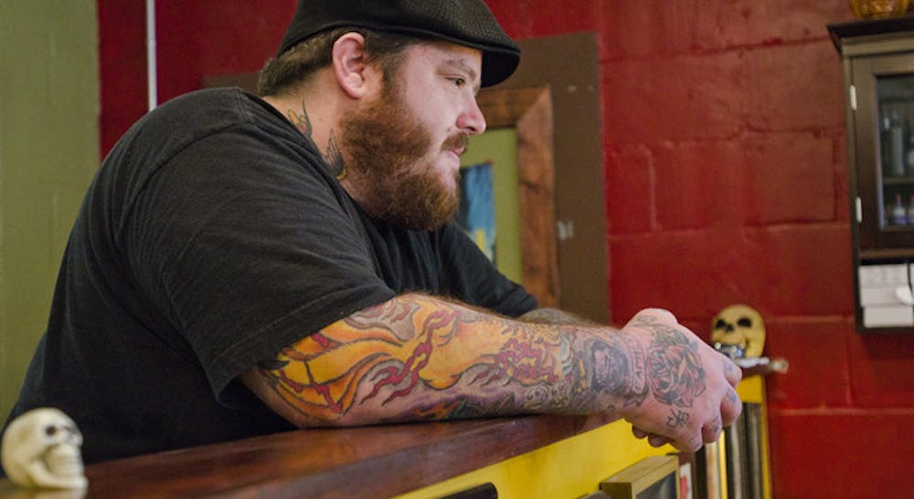 <p>Mike Mehaffey, owner of Death or Glory Tattoo Parlour at 2224 NW Sixth St., looks on as coworker Robert Barnes tattoos a client (not pictured). The duo, who go by Little Mike and Ol' Dirty Rob, are two of the main tattoo artists at Death or Glory, which Mehaffey opened just a few weeks ago after leaving Anthem Tattoo Parlor earlier this year. Death or Glory hasn't had a grand opening yet, but Mehaffey said his goal is to run an "old-school street shop," where his loyal clientele is treated like family. Mehaffey's shop provides a more wholesome and welcoming alternative to quick, cheap tattoo shops such as Body Tech.</p>