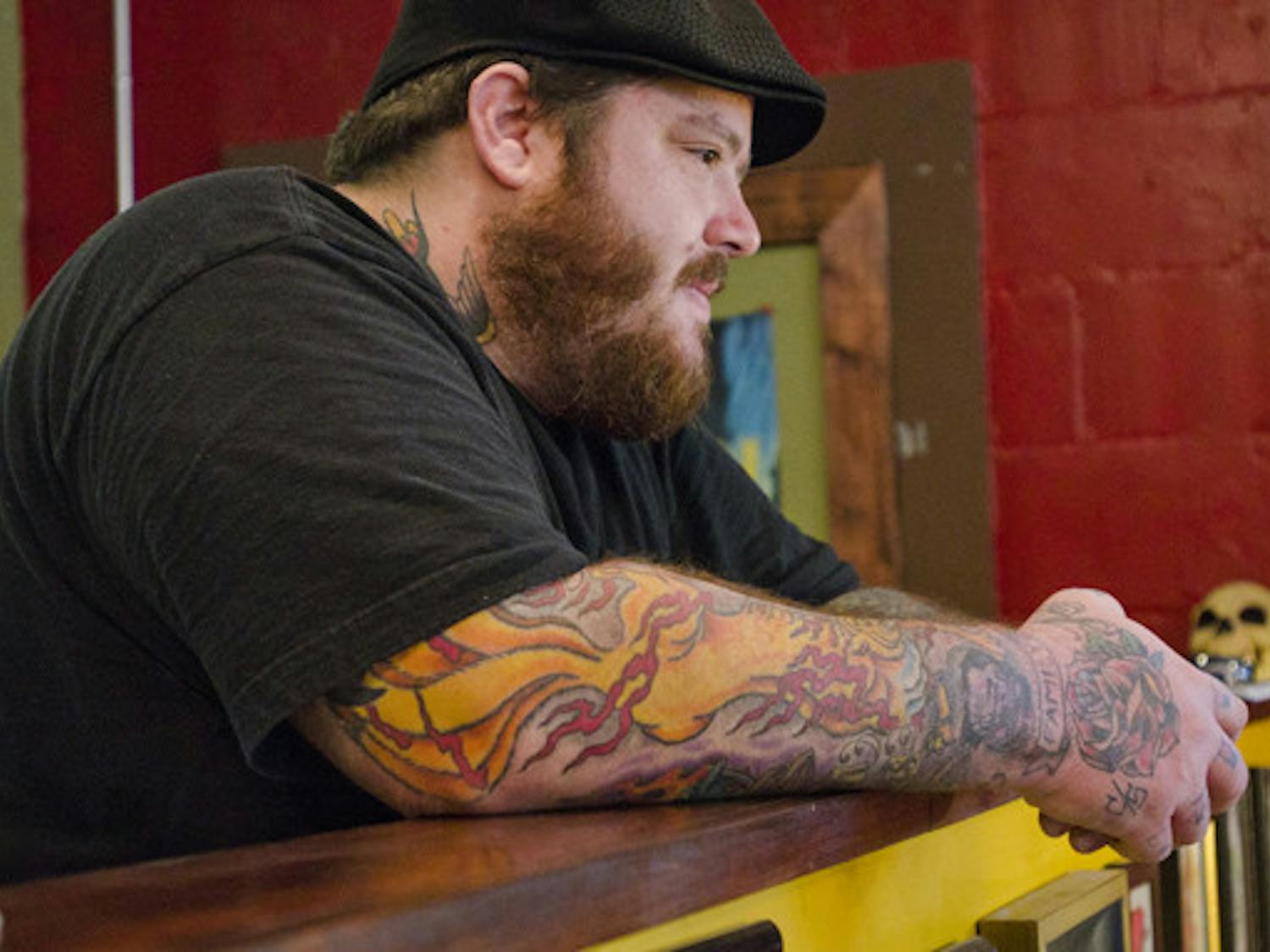 Mike Mehaffey, owner of Death or Glory Tattoo Parlour at 2224 NW Sixth St., looks on as coworker Robert Barnes tattoos a client (not pictured). The duo, who go by Little Mike and Ol' Dirty Rob, are two of the main tattoo artists at Death or Glory, which Mehaffey opened just a few weeks ago after leaving Anthem Tattoo Parlor earlier this year. Death or Glory hasn't had a grand opening yet, but Mehaffey said his goal is to run an "old-school street shop," where his loyal clientele is treated like family. Mehaffey's shop provides a more wholesome and welcoming alternative to quick, cheap tattoo shops such as Body Tech.